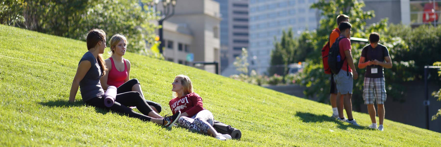 Student gather after a work out to talk on a grassy hill.